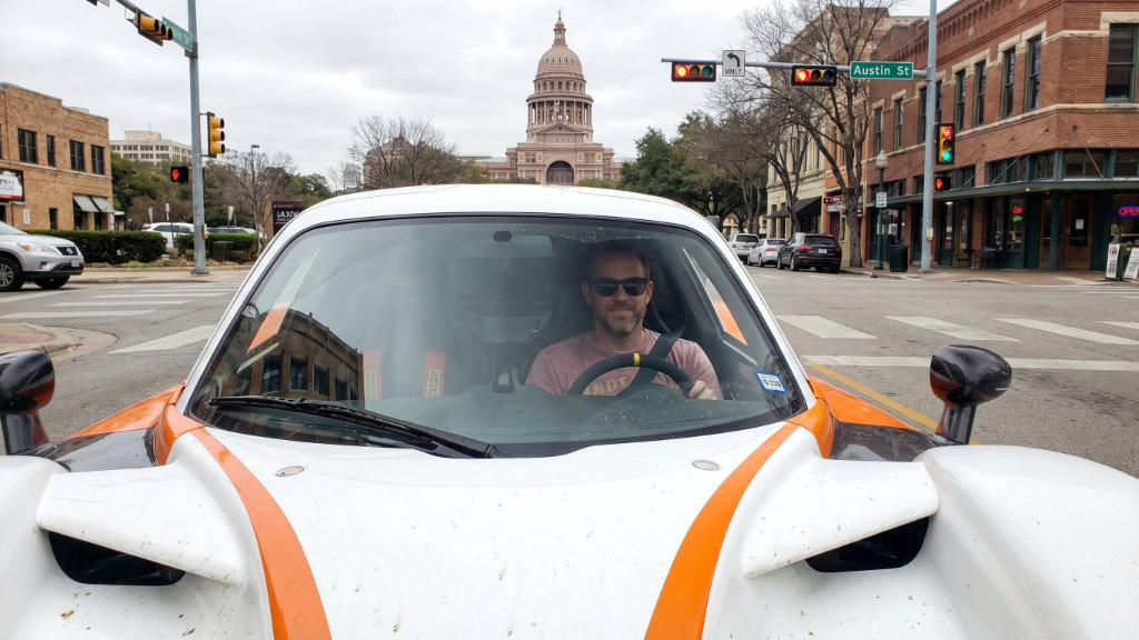 Man driving white and orange sports car through Austin street with Capitol building backdrop