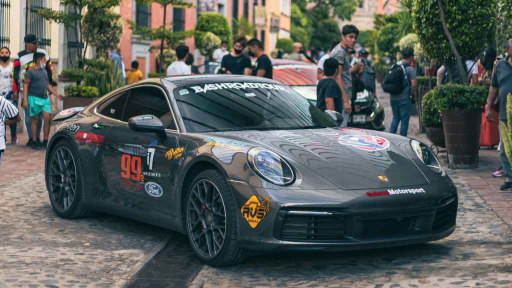 Gray Porsche 911 sports car displayed at Mexican street car show with colorful colonial buildings and spectators